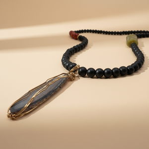 Necklace with black beads and a large blue stone pendant on a beige background