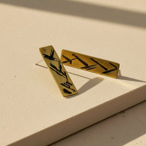 Gold earrings with black designs on a beige surface