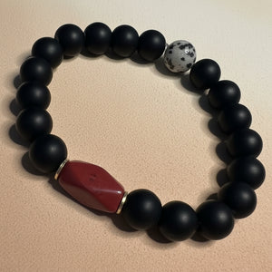 Black beaded bracelet with a red stone on a white background
