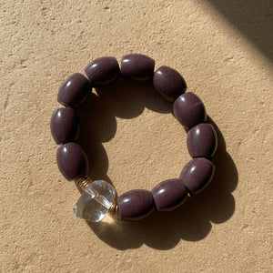 Bracelet with dark beads and a clear crystal bead on a beige background