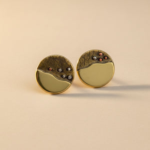 A pair of earrings with a gold-colored textured surface and a polished, silver-colored layer on top, featuring red and nickel accents.