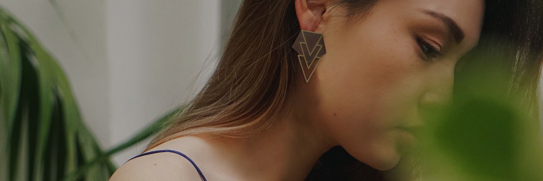 A woman is wearing earrings in upcycled leather and brass amongst foliage.