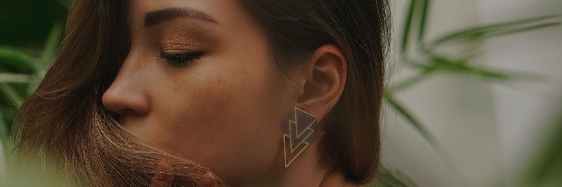 A woman is wearing earrings in upcycled leather and brass amidst foliage.