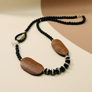 Necklace with black beads, wooden pendants, and white accents on a beige background