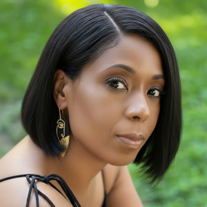 Woman with a short black hairstyle wearing gold earrings against a green background