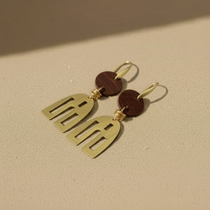 Gold earrings with leather accents on a beige surface