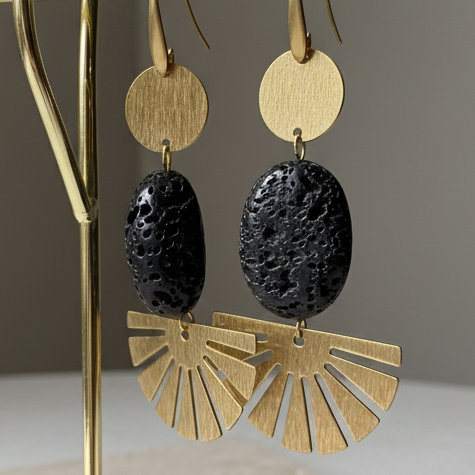 Gold and black earrings on a gold earring stand with a beige base, against a neutral background.
