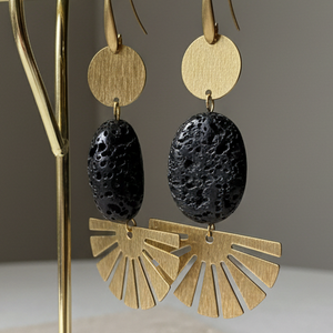 Gold and black earrings on a gold earring stand with a beige base, against a neutral background.