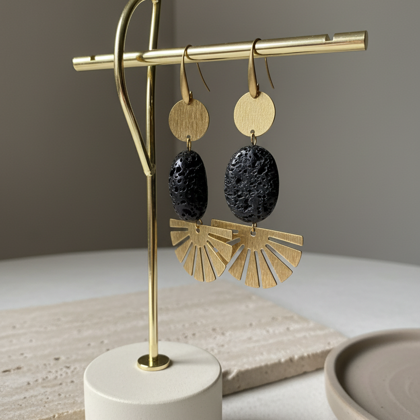 Gold and black earrings on a gold earring stand with a beige base, against a neutral background.