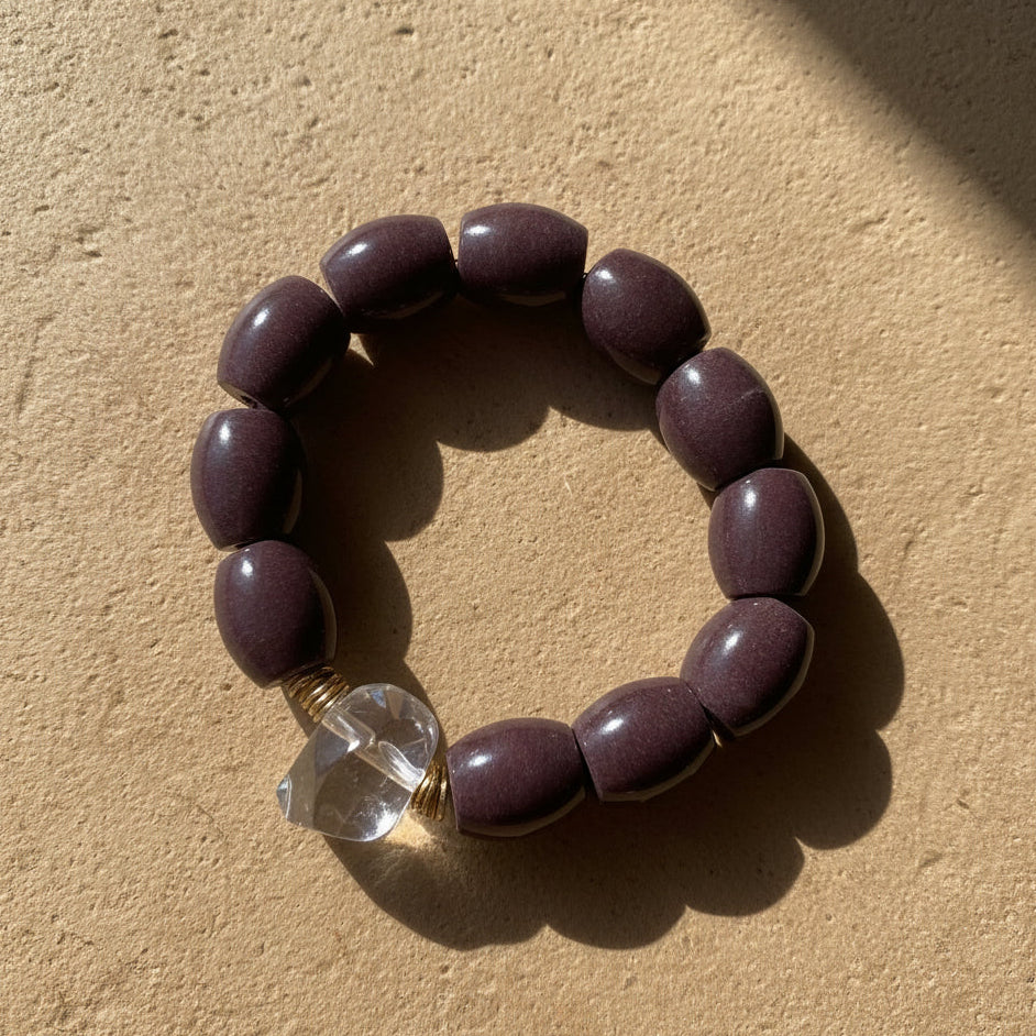 Bracelet with dark beads and a clear crystal bead on a beige background