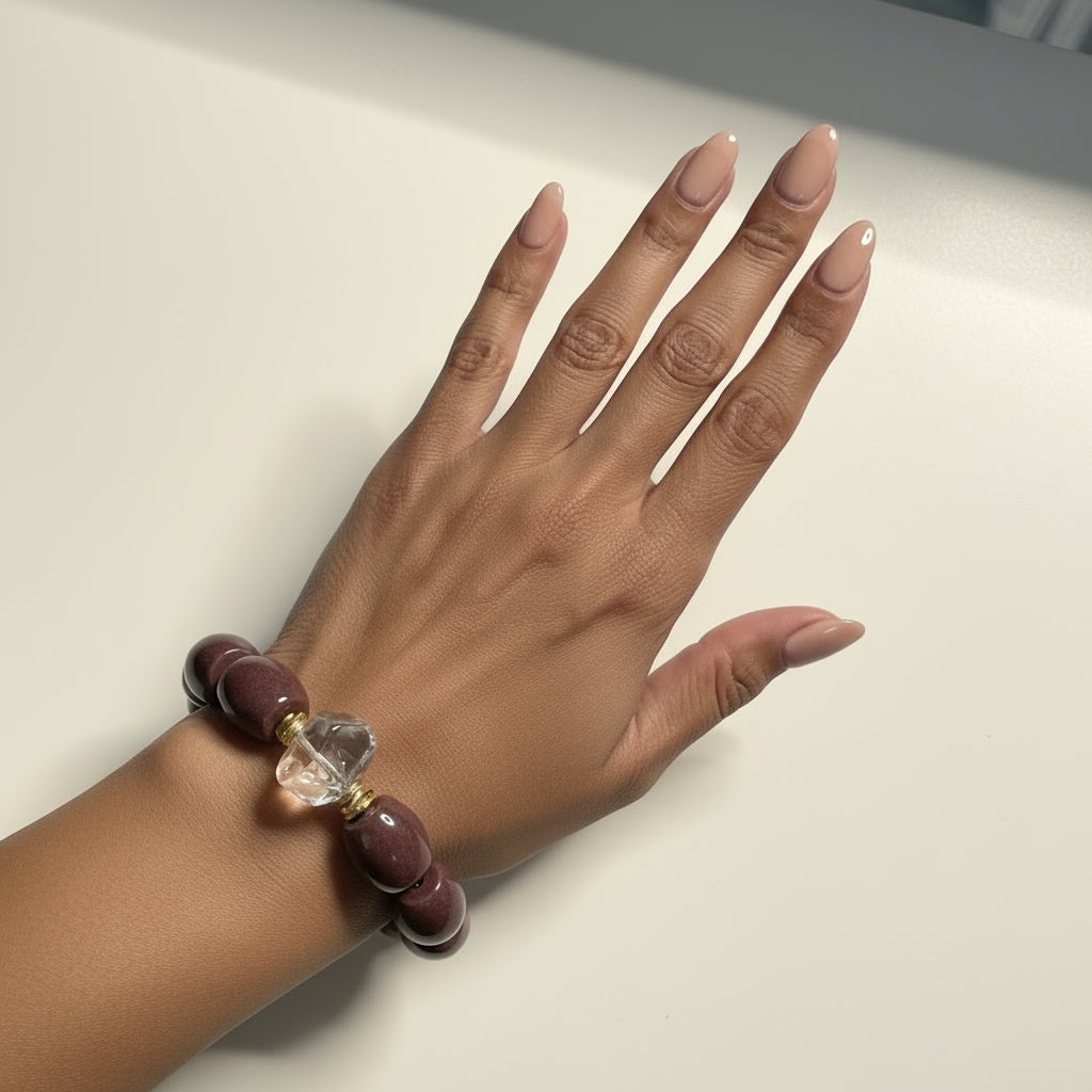 Bracelet with brown beads and a clear crystal on a wrist against a light background