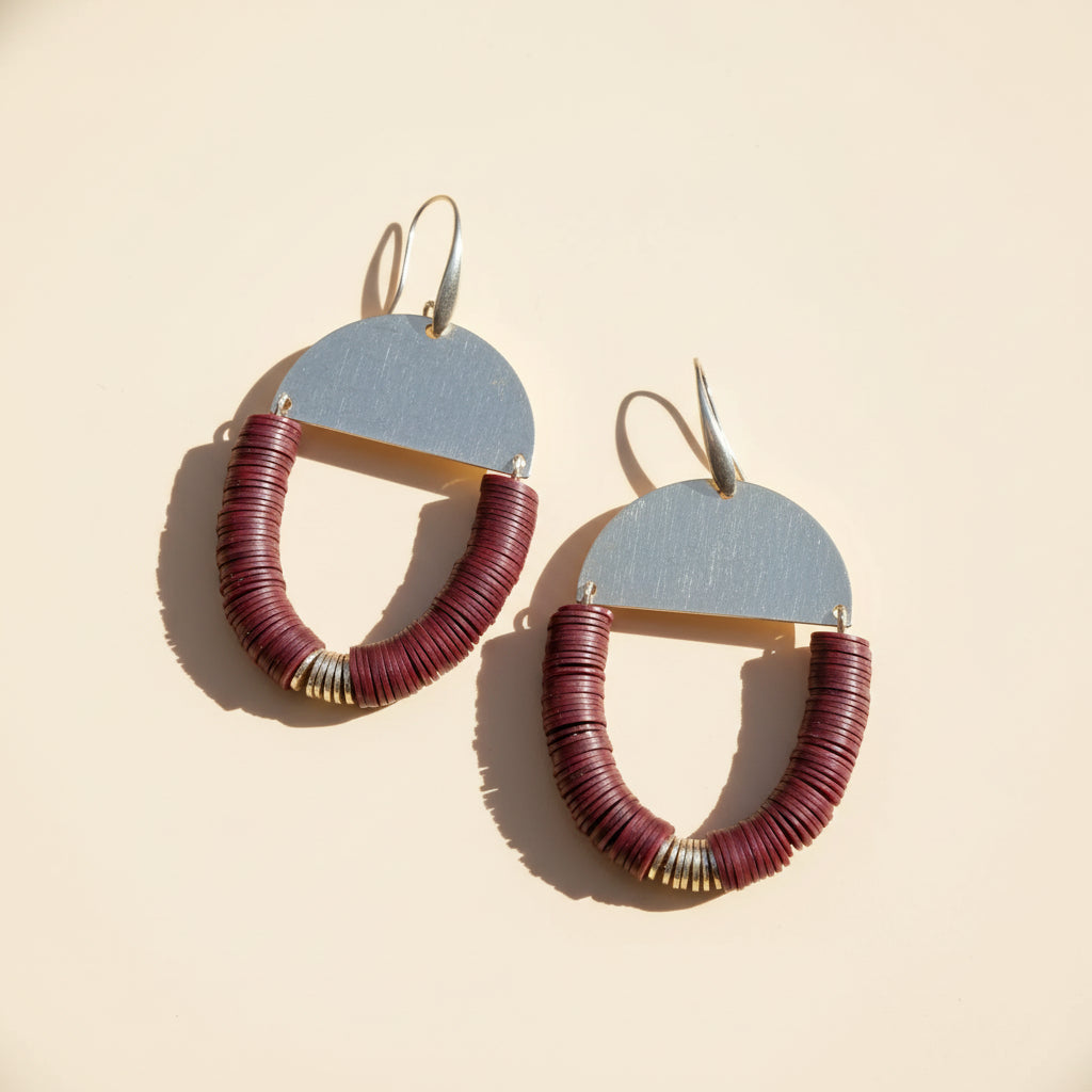 Pair of earrings with burgundy circular designs on a wooden surface
