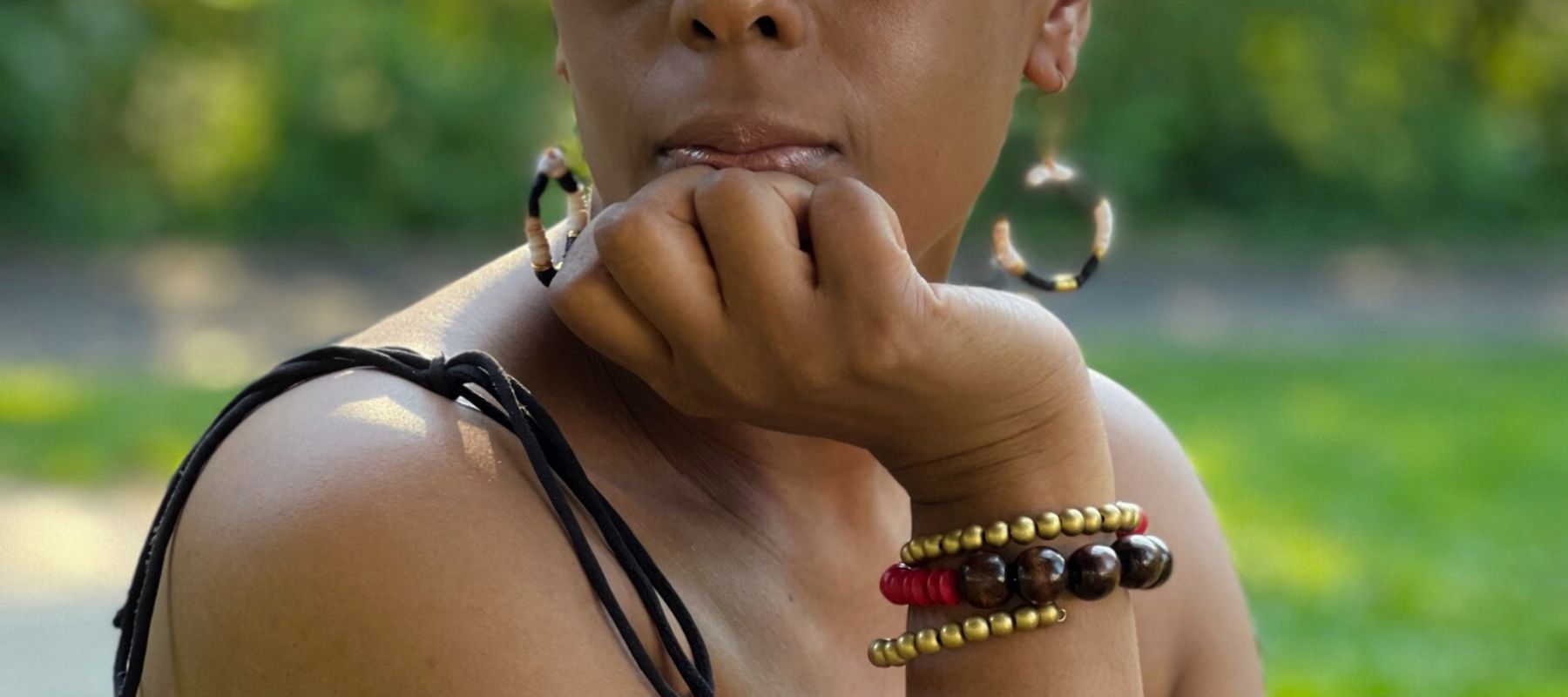 A woman is wearing brass hoop earrings and a beaded wrap bracelet.